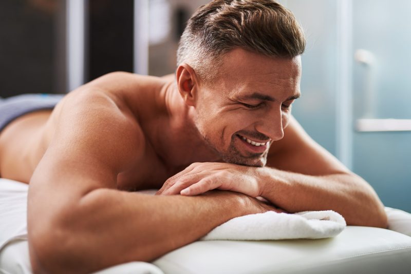 Attractive unshaven gentleman relaxing at spa salon. He resting chin on hands and smiling